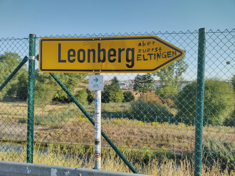Offizeille Beschilderung 'Leonberg' und auf das Schild hat jemand geschrieben 'aber zuerst ELTINGEN'.
