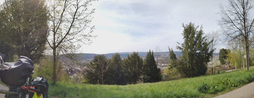 Über Bäume im Park unterhalb des Betrachters hinweg sind die Stadt Pforzheim und die Hügel dahinter sichtbar.
