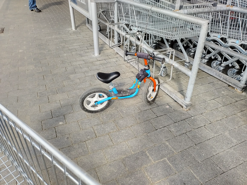 Ein Laufrad für Kinder steht an einem Felgenbrecher vor einem Einkaufsmarkt