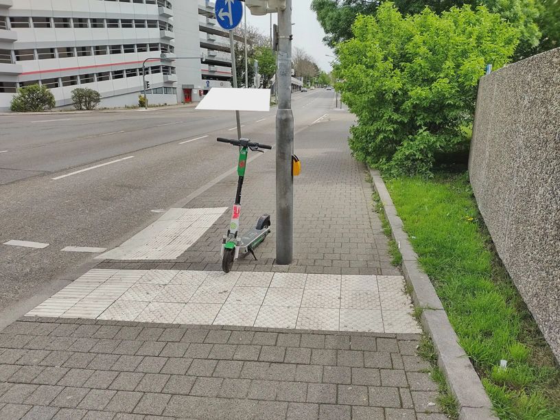 E-Roller auf einem Leitsystem für blinde Menschen mitten an einem Fußgängerüberweg.