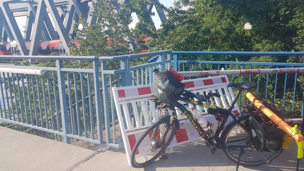 Mein Fahrrad auf der Brücke in Karlsruhe, die über den Rhein führt. Das Fahrrad steht vor dem Brückengeländer, dahinter eine Zugbrücke mit einem gerade darauf fahrenden Zug.